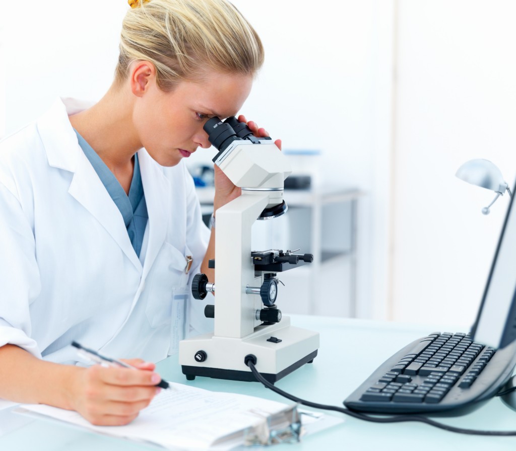 Young female researcher looking into a microscope and writing notes at laboratory